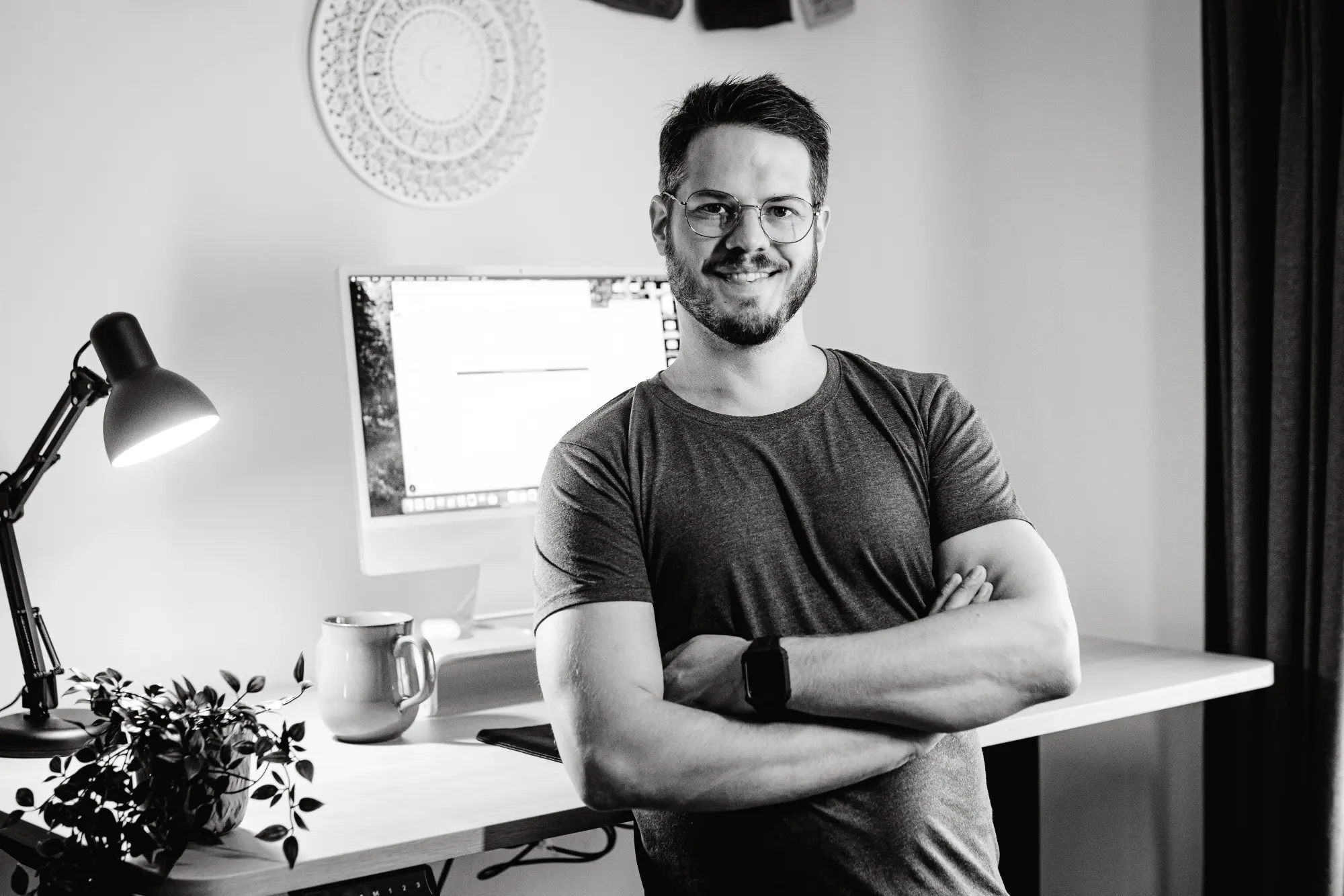 Carsten Kien steht mit einem warmen Lächeln und verschränkten Armen vor seinem Schreibtisch.